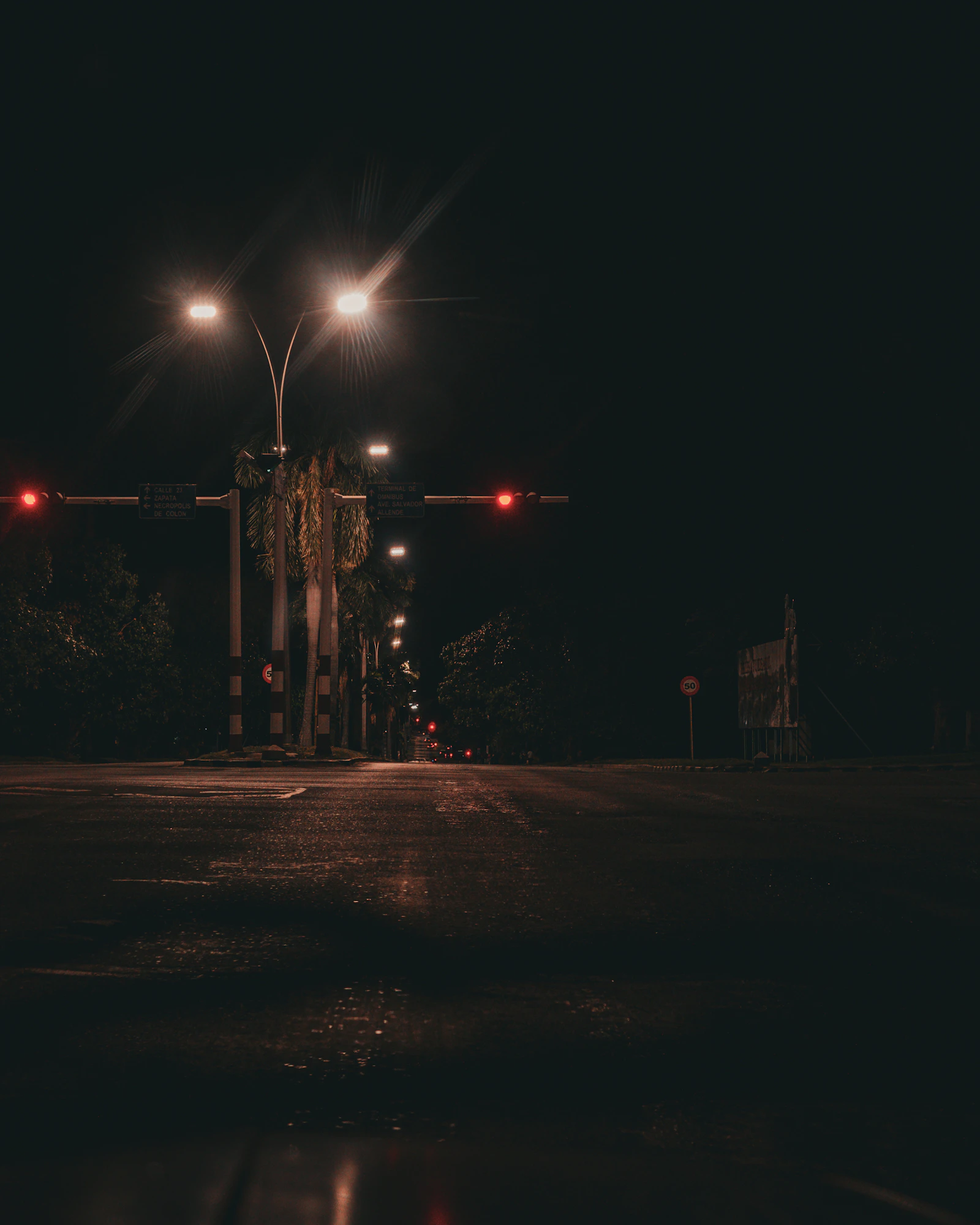 A largely dark Havana road at night, punctuated by streetlights and red traffic signals.